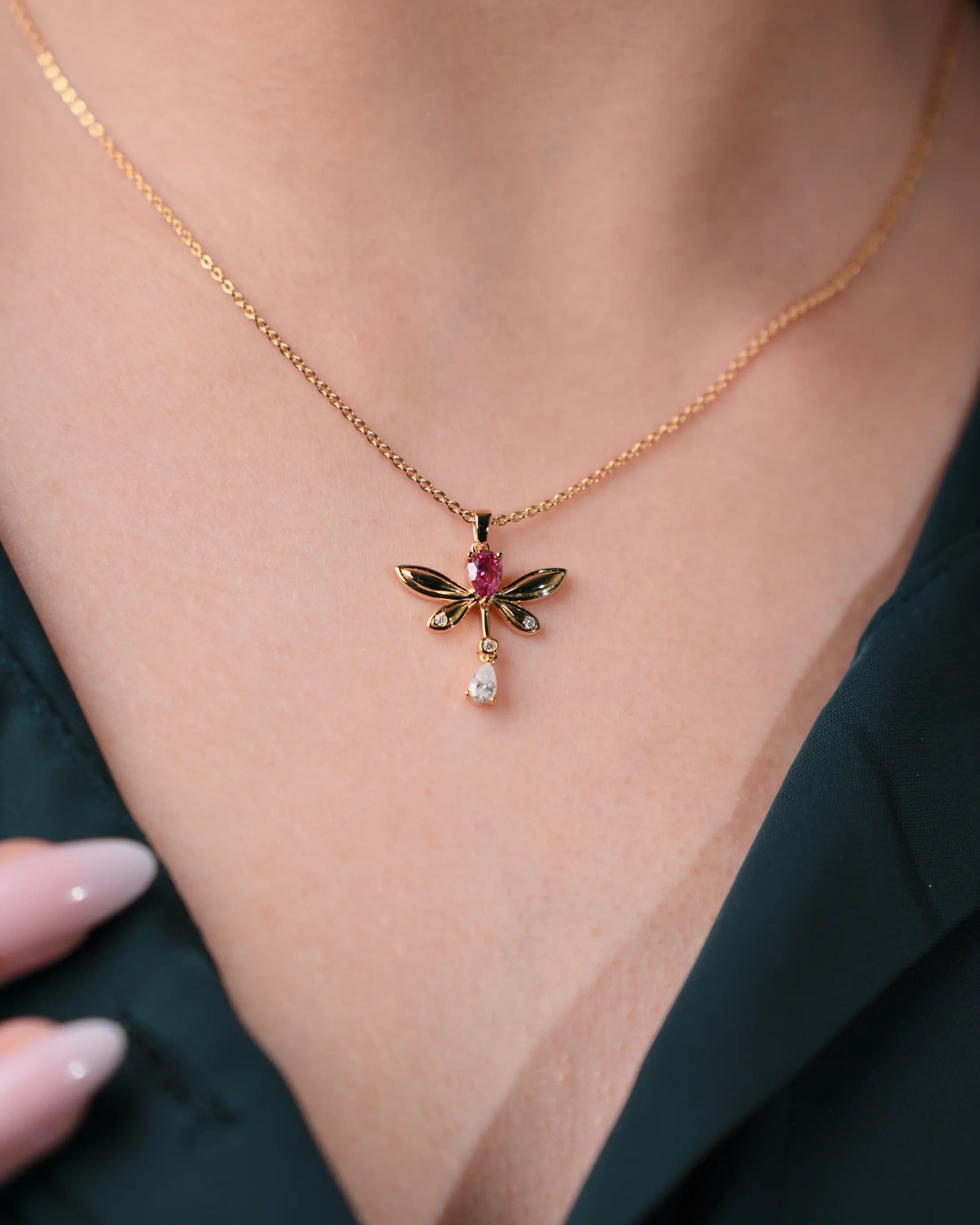 Gold necklace with a dragonfly pendant featuring gemstones on a person's neck.
